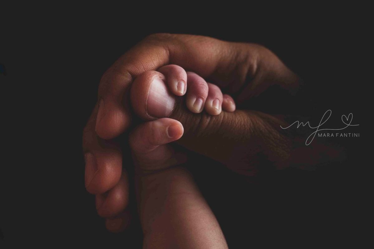 Foto neonato piedini in studio a Roma | Mara Fantini Primo piano dei piedini del neonato tra le mani del papà, servizio fotografico in studio