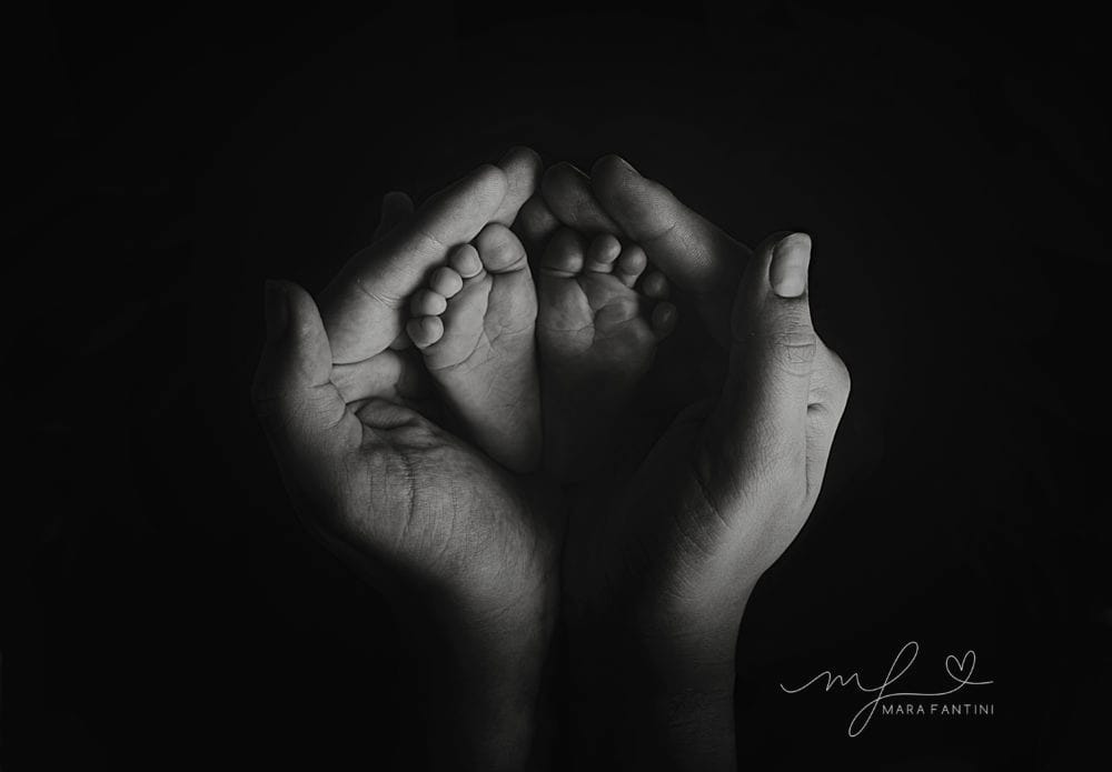 Foto neonato piedini mani genitori - studio Roma | Mara Fantini Mani dei genitori a coppa intorno ai piedini del neonato, foto in bianco e nero in studio