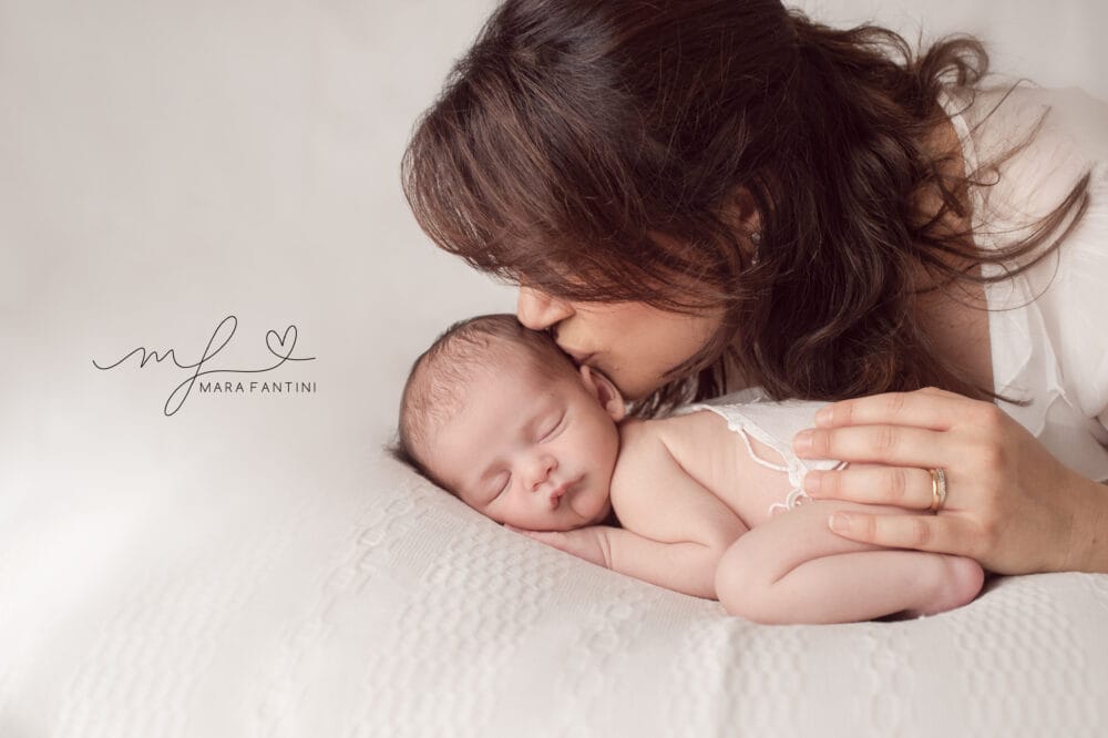 mamma-bacio-neonato-toni-chiari-studio-roma.jpg Mamma bacia sulla fronte il neonato addormentato, servizio fotografico in studio dai toni chiari