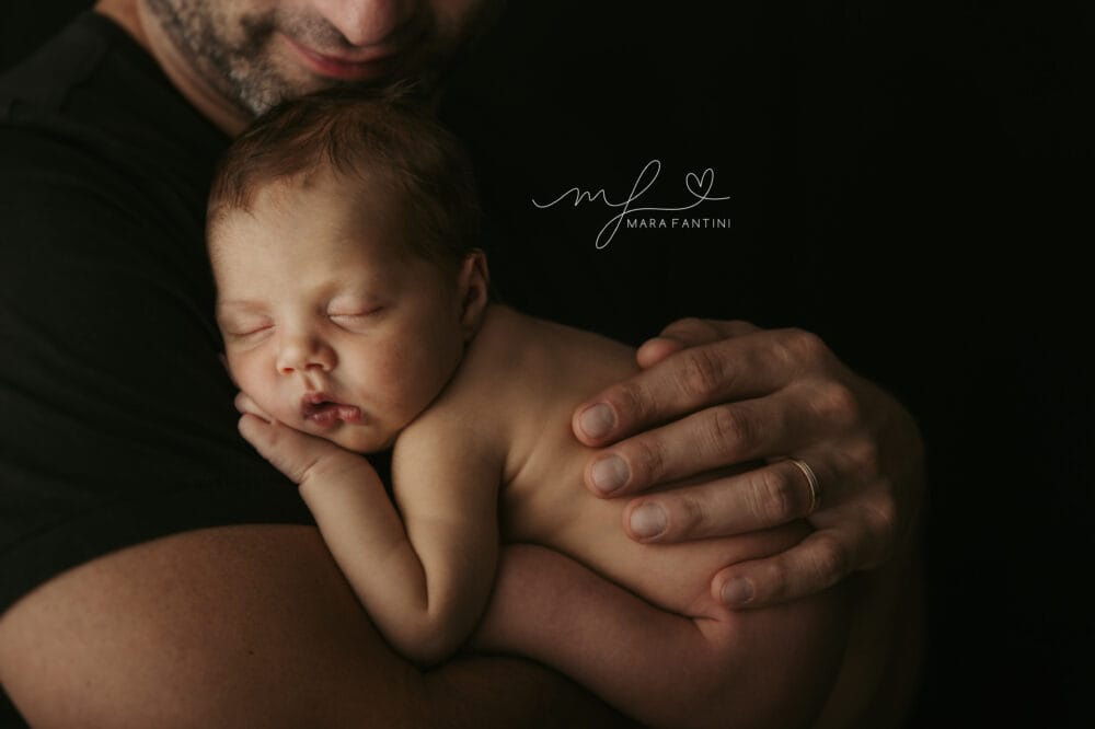 neonato-papa-braccia-studio-roma.jpg papà tiene il neonato addormentato tra le braccia durante il servizio fotografico in studio a Roma