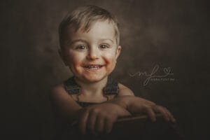 Bambino sorridente durante un servizio fotografico a Roma, sfondo scuro dal tocco pittorico, momento spontaneo e naturale