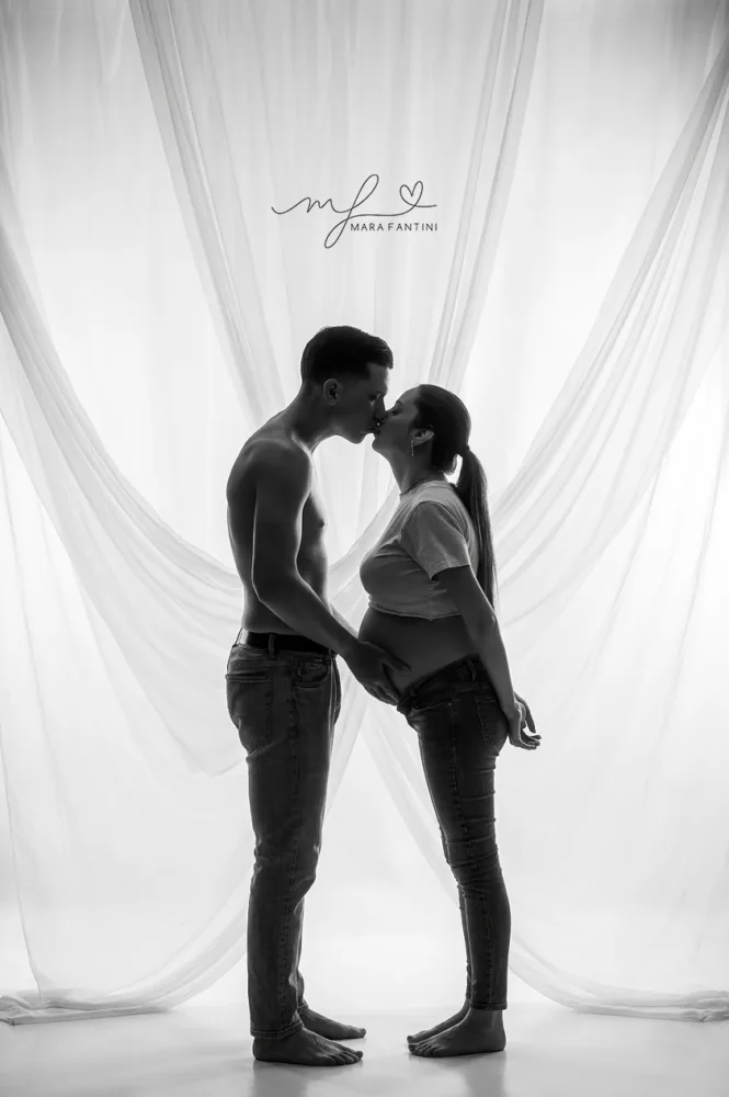 Foto di gravidanza artistica in bianco e nero in controluce, con un bacio intimo tra la futura mamma e il partner in uno studio fotografico a Roma.