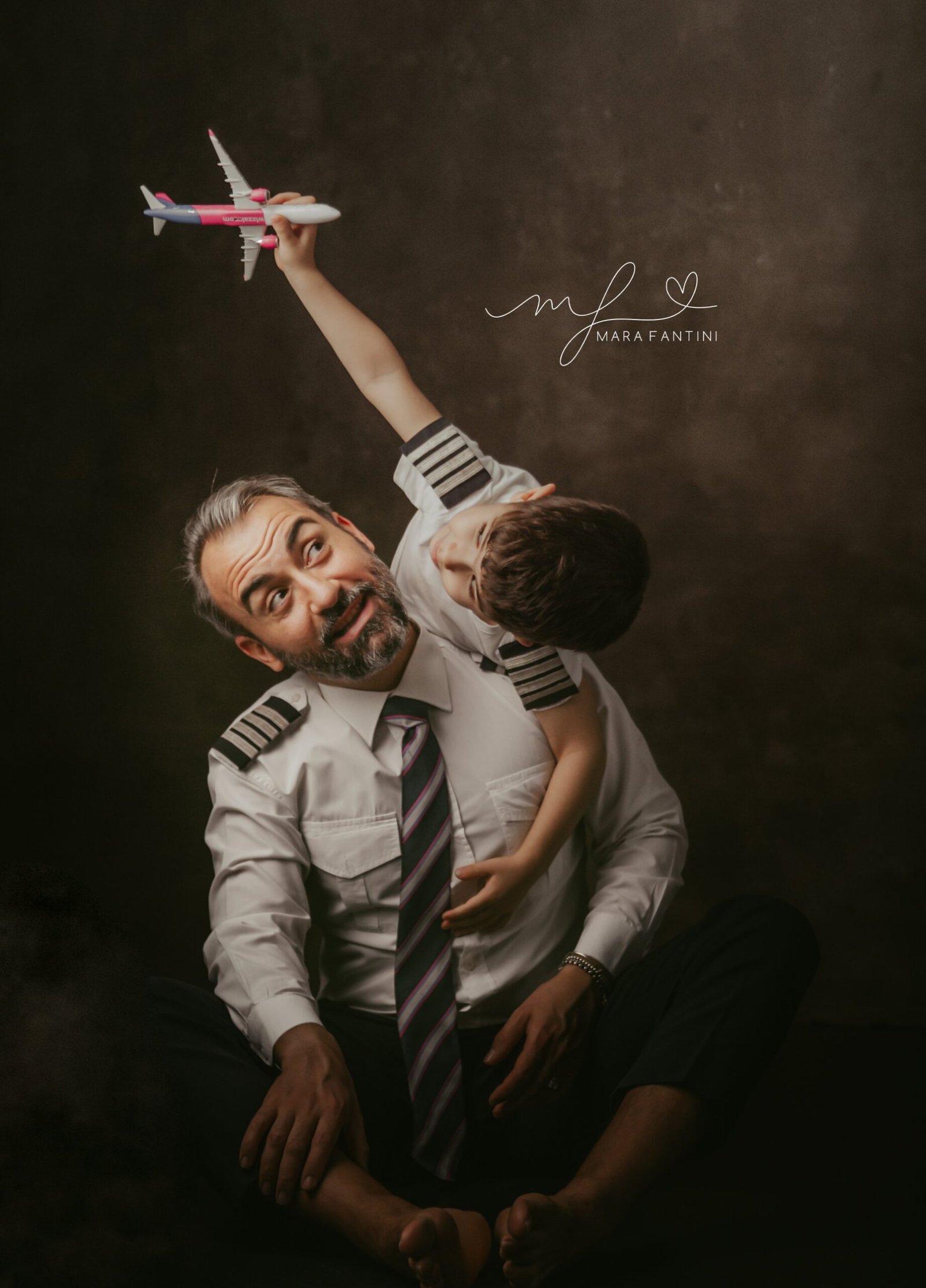 Papà pilota e figlio con aeroplanino in alto Bambino in braccio al papà pilota solleva un aeroplanino verso l'alto mentre il papà lo guarda con una smorfia divertita